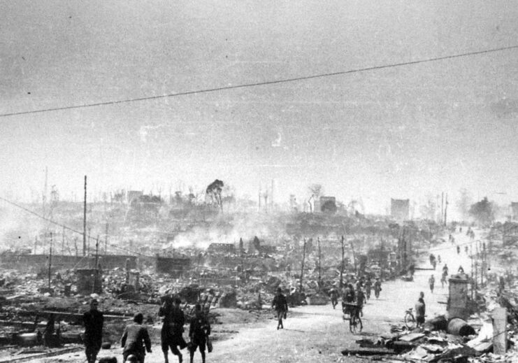 Japanese civilians walk along a street surrounded by destroyed buildings