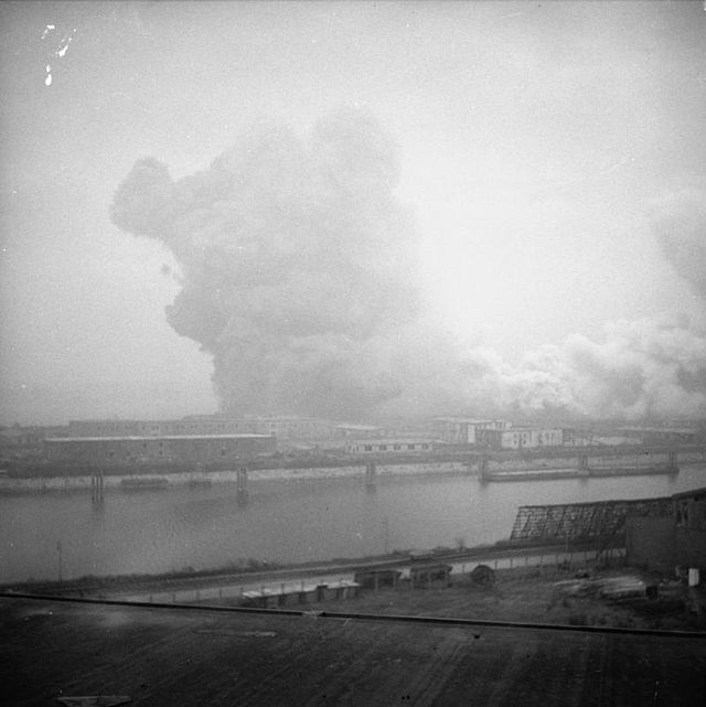 Cloud of smoke rising into the air, as seen from across a waterway