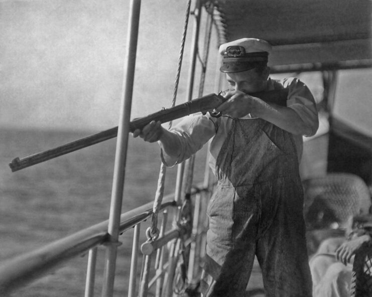 Jacob Martin aiming a rifle while aboard a ship at sea