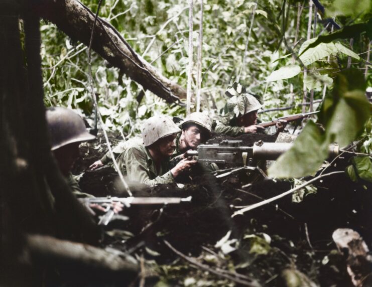 Four Marines looking through guns in the middle of a wooded area. 