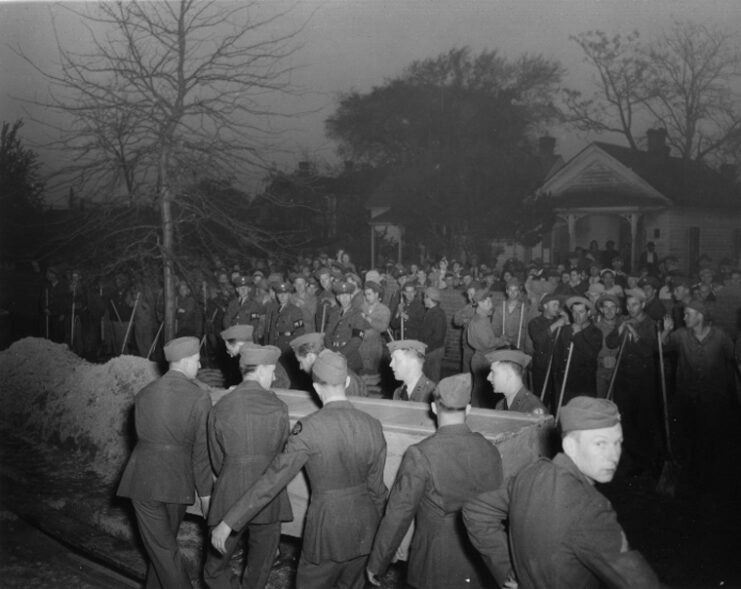 US Navy sailors and civilians watching as more sailors carry a coffin on a dark night