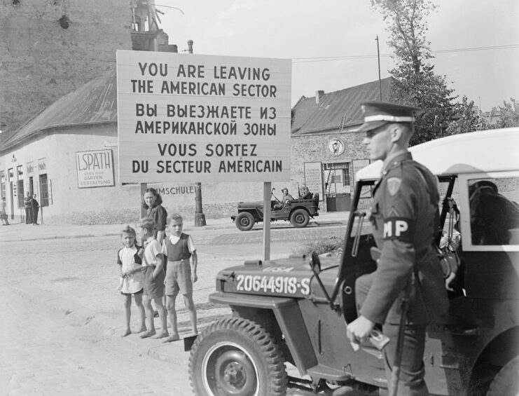 Family and military police officer standing near a sign in the American Occupation Zone