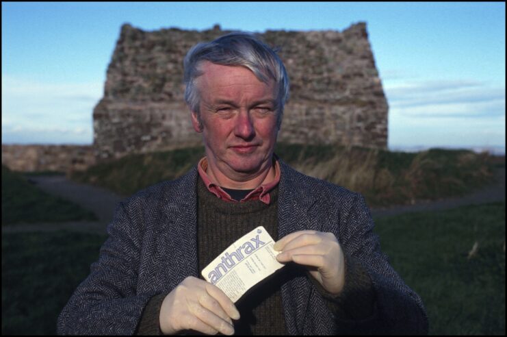 Man standing holding a page that reads 'ANTHRAX' on Gruinard island.