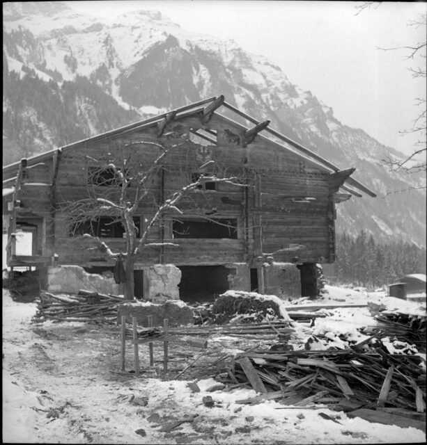 Exterior of a broken chalet, with debris strewn around it