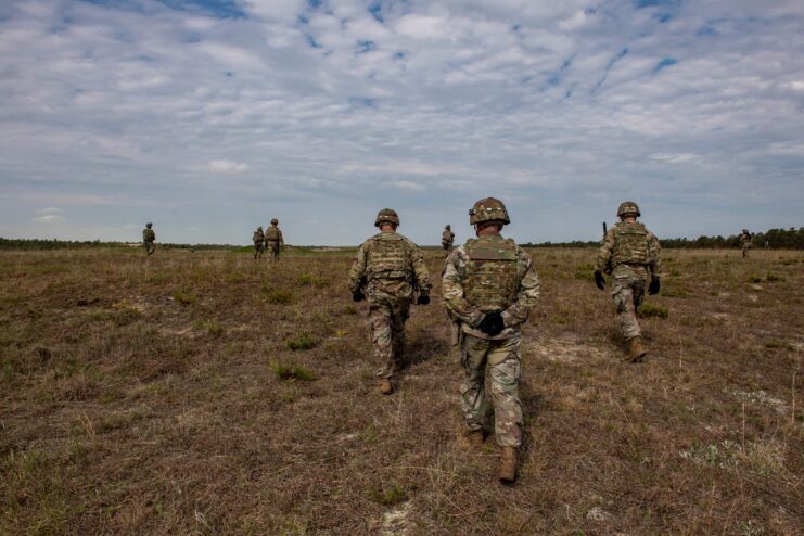 Officers watch as members of the 182d Infantry Regiment work in concert as small squads and fire on targets in a field during training. 