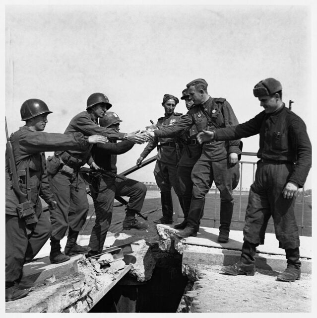 American and Soviet soldiers reaching out to shake each other's hands