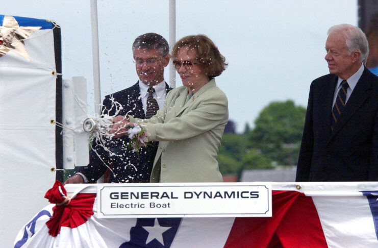 Rosalynn Carter breaking a bottle of champagne off the deck of the USS Jimmy Carter (SSN-23), while Jimmy Carter and John P. Casey watch