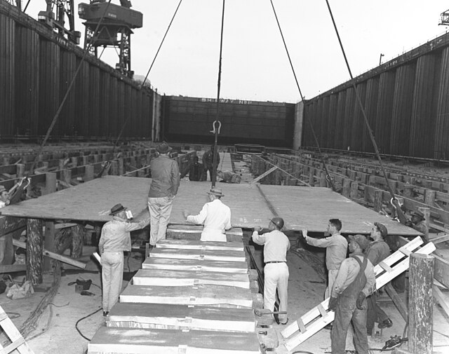 Workmen laying the keel plate of the USS United States (CVA-58) in dry dock