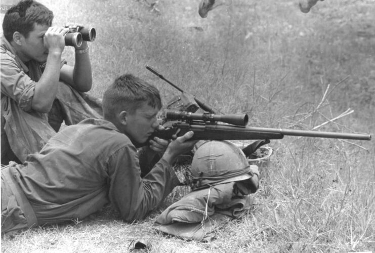 US Marine sniper aiming his rifle while another looks through a pair of binoculars