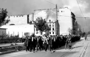 Polish civilians being led down a street while German soldiers stand guard