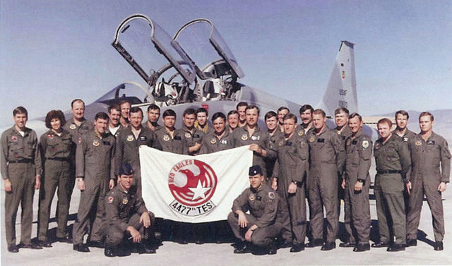 Airmen with the 4477th Test & Evaluation Squadron "Red Eagles" standing with a flag bearing their insignia