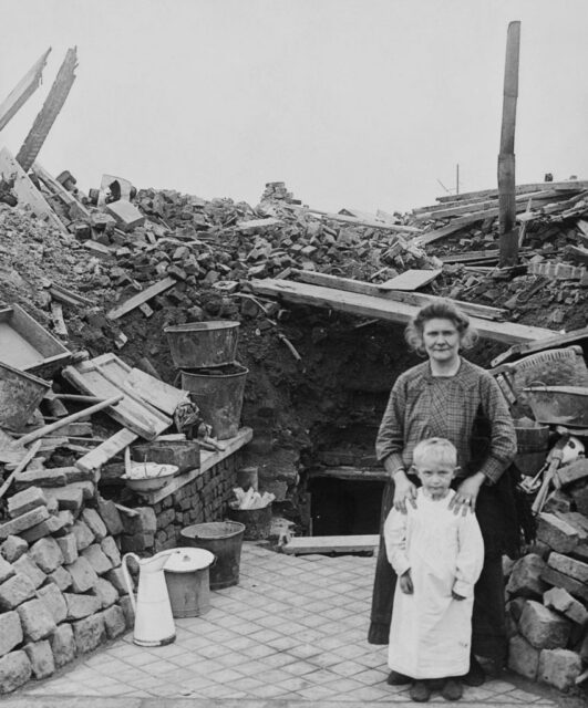 Mother and child standing in front of the ruins of a house