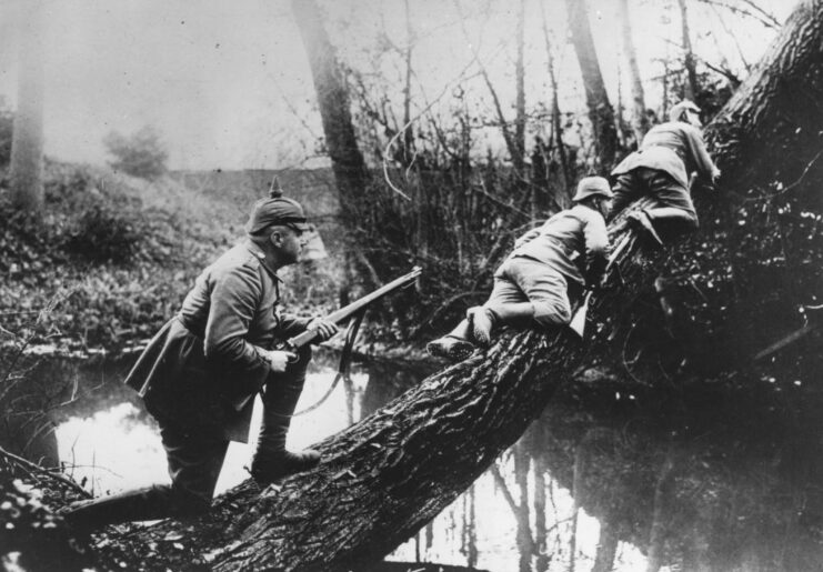 Three German soldiers climbing up a downed tree trunk