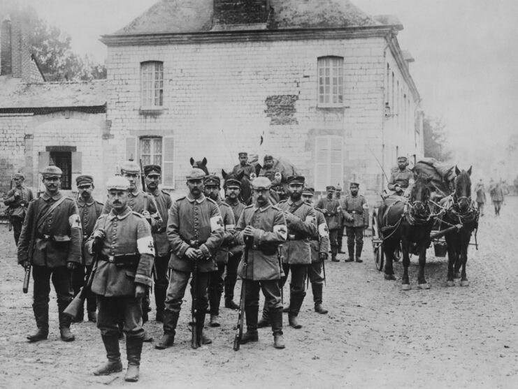 Infantry medics from the Imperial German Army Medical Service wearing Red Cross armbands, and carrying Mauser Gewehr 98 bolt action rifles at a field hospital.