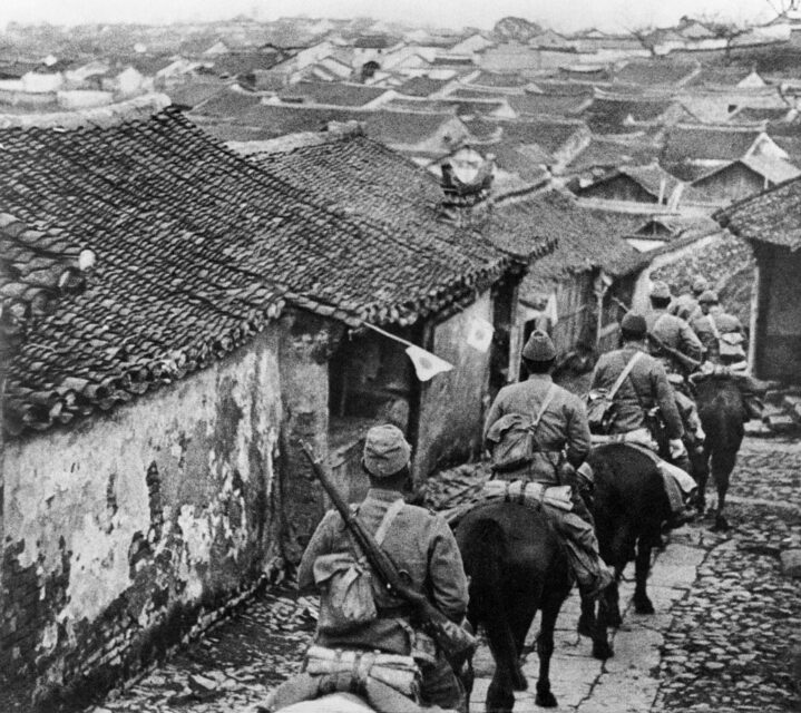 Japanese soldiers riding through a village on horseback