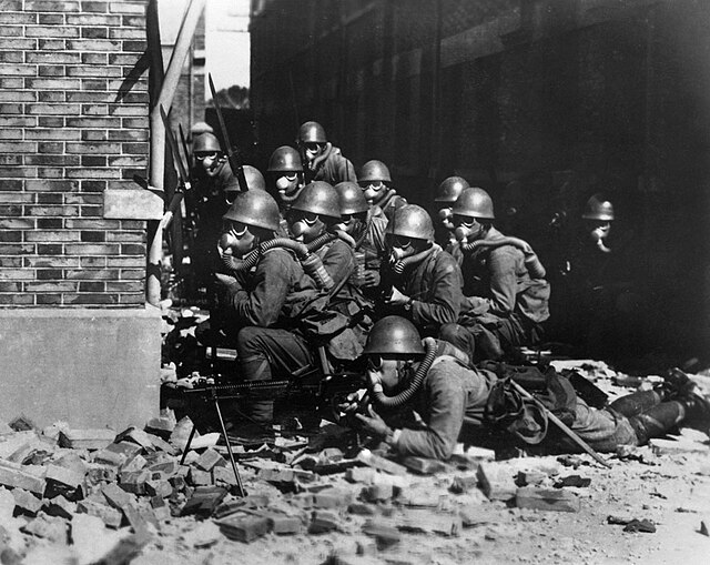 Imperial Japanese Navy (IJN) Special Naval Landing Force members crouched together behind a building