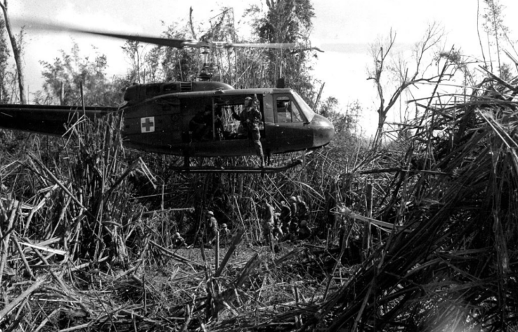 Bell UH-1 Huey hovering over ground troops in the middle of a grassy area