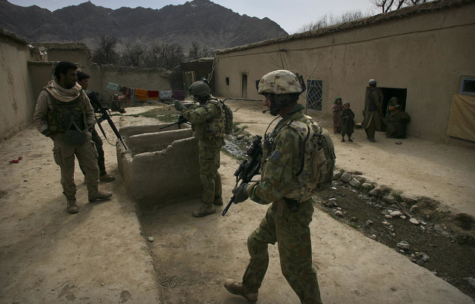 Soldiers walking near a building, while a family stands nearby