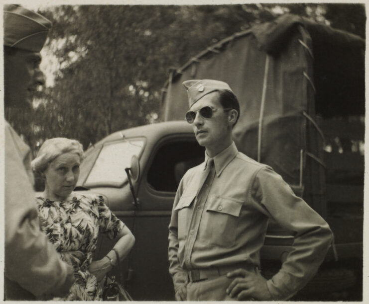 Soldier in uniform and aviator sunglasses with another soldier and civilian woman.