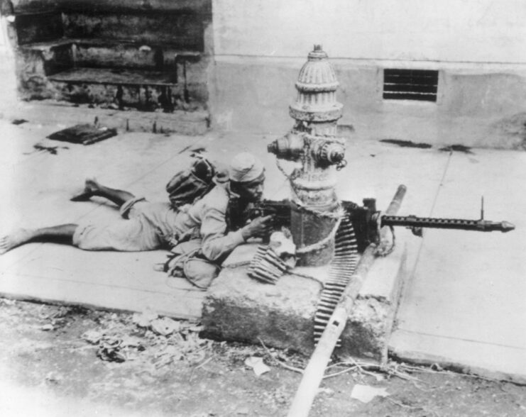 Filipino guerrilla lying behind a fire hydrant while aiming his rifle