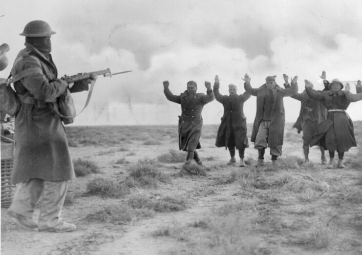 Group of Italian troops walking toward an Australian soldier with their arms raised over their heads in surrender