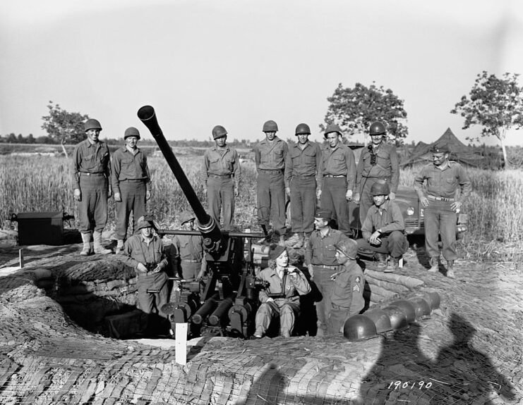 Marlene Dietrich sitting at an artillery weapon, with its crew standing around her