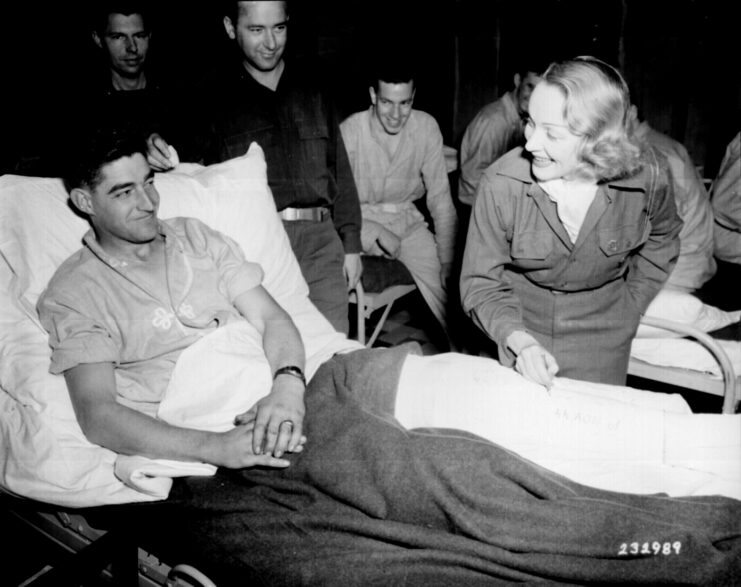 Marlene Dietrich leaning over Earl E. McFarland's bed, while other service members stand nearby