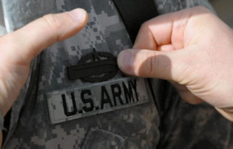 Close-up of hands pinning the Combat Infantry Badge (CIB) onto a US Army soldier's uniform