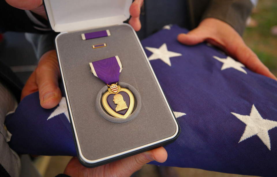 Hands holding a Purple Heart and a folded American flag