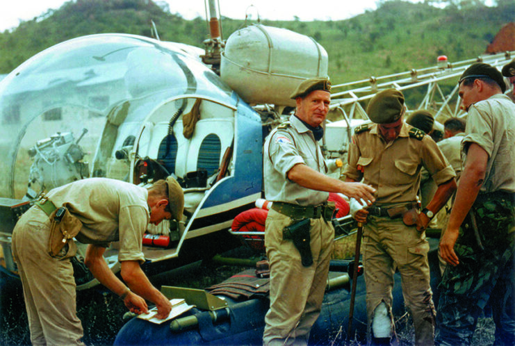 Mike Hoare, John Peters and other mercenaries standing around a helicopter