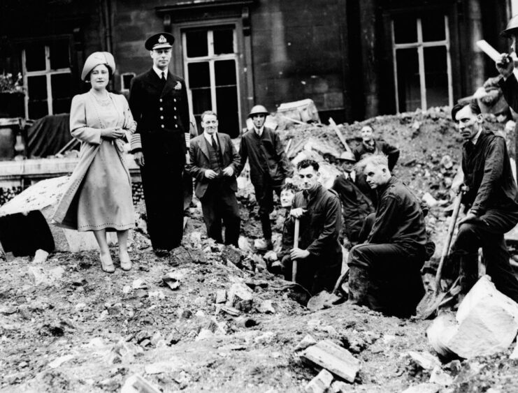 King George VI and Elizabeth, the Queen Mother standing with workers in a pile of rubble