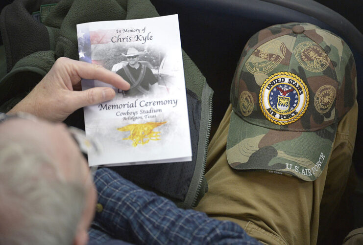 Man holding a funeral pamphlet and balancing a baseball cap on his knee