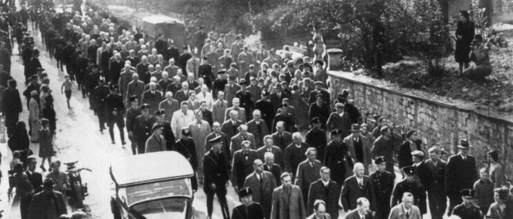 Lines of Jewish individuals being led down a street by SS officers