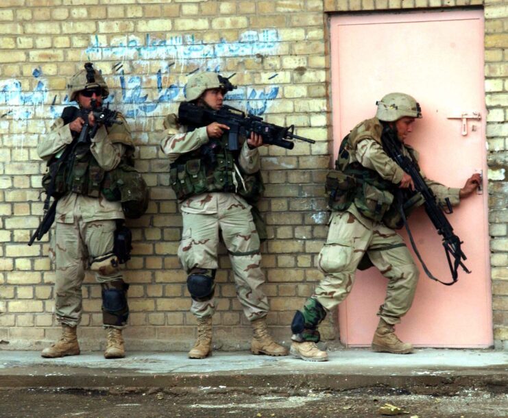 Three US Army soldiers with their backs against a brick wall