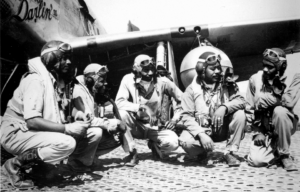 Five Tuskegee Airmen kneeling next to an aircraft