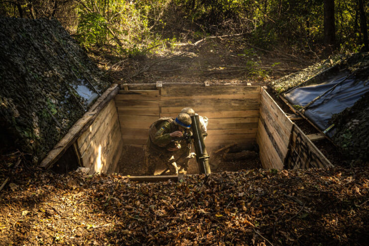 Two Ukrainian soldiers standing with a 120 mm mortar in a hole in the ground