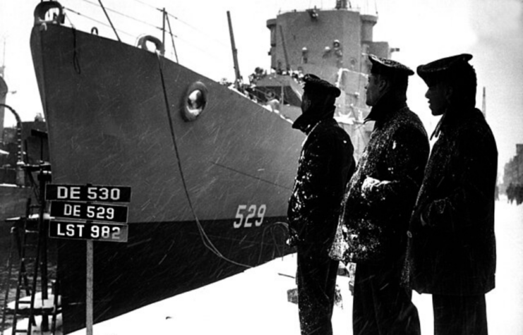 Three sailors standing near the docked USS Mason (DE-529)